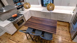 Overhead view of a newly remodeled kitchen featuring two-toned cabinetry, a large natural wood island, exposed brick, black windows, and pendant lights.