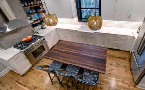 Overhead view of a newly remodeled kitchen featuring two-toned cabinetry, a large natural wood island, exposed brick, black windows, and pendant lights.