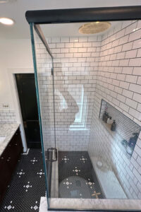 View of the glass enclosed shower in a custom tiled black and white bathroom.
