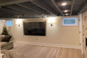 View of a lower level family room featuring an open, painted ceiling and sunken television wall.