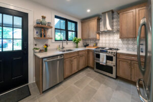View of newly remodeled kitchen with wood cabinets, backsplash tile, and floating shelves.