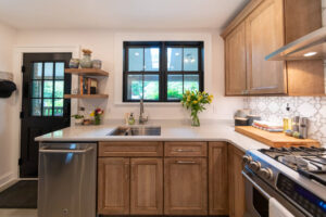View of newly remodeled kitchen with wood cabinets and floating shelves.