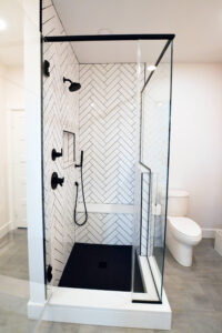 Open door view of the modern black and white tiled shower in a newly remodeled bathroom.