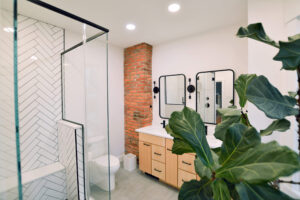 View of an updated bathroom in Shadyside near Pittsburgh. The newly expanded space features warm earth tones, an exposed brick wall, modern black and white tiled shower, and tons of natural light.