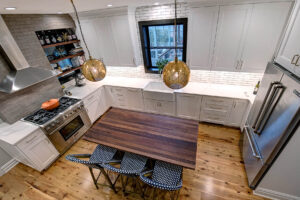 Overhead view of a newly remodeled kitchen featuring two-toned cabinetry, a large natural wood island, exposed brick, black windows, and pendant lights.