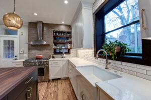 View of a newly remodeled kitchen featuring two-toned cabinetry, a large natural wood island, exposed brick, black windows, and pendant lights.