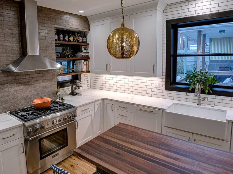 View of a newly remodeled kitchen featuring two-toned cabinetry, a large natural wood island, exposed brick, black windows, and pendant lights.