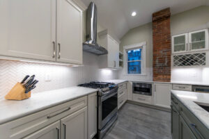 View of a remodeled classic white kitchen with marble countertops, herringbone tile backsplash, and built-in wine storage.