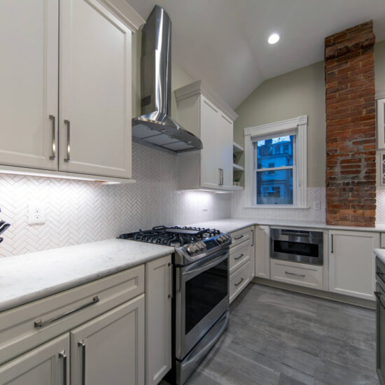 View of a remodeled classic white kitchen with marble countertops, herringbone tile backsplash, and built-in wine storage.