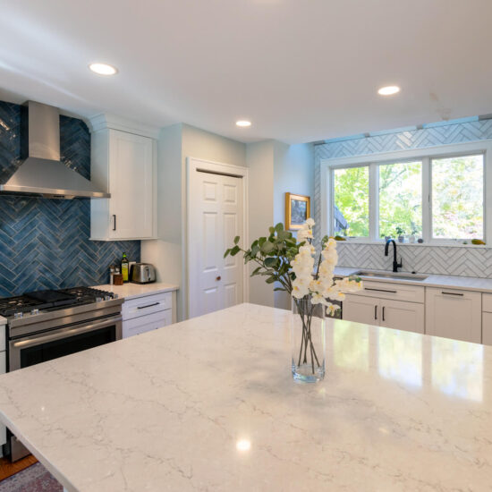 Close up of the large island in a newly remodeled kitchen featuring white cabinetry and marble countertops.