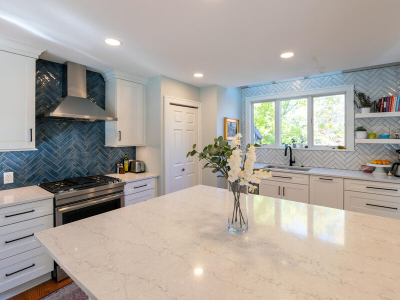 Close up of the large island in a newly remodeled kitchen featuring white cabinetry and marble countertops.