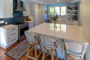 View of a newly remodeled kitchen featuring white cabinetry, marble countertops, and blue backsplash tile.