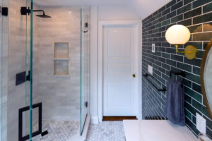 Broad view of a recent bathroom renovation in Pittsburgh that includes a wood vanity, tile floor, custom corner shower, and floating shelves.