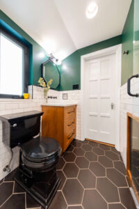 Broad view of a bathroom with green walls, black and white tile, a walk-in shower, and wood vanity.