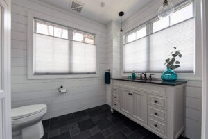 View of powder room with shiplap walls, a large-format tile floor, and big windows.