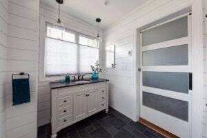 View of sink in a Pittsburgh powder room with shiplap walls, a large-format tile floor, and big windows.