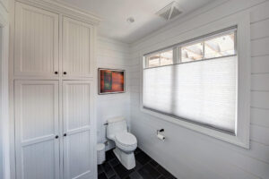 View of large windows in a recently remodeled powder room with shiplap walls and a large-format tile floor.