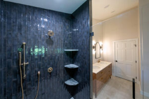 View of a beautifully remodeled bathroom from inside the spacious walk-in shower with blue tile and gold fixtures.