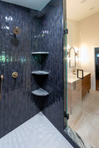 View of a beautifully remodeled bathroom from inside the spacious walk-in shower with blue tile and gold fixtures.