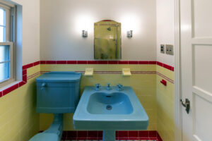 View of a renovated bathroom with vintage style tiled walls and blue ceramic sink and toilet.
