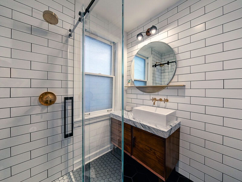 View of a sleek bathroom with white subway tile, glass shower enclosure, and modern vanity.