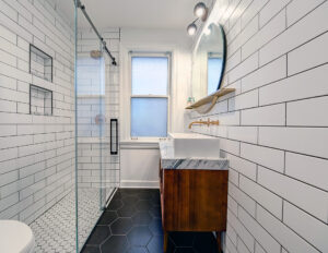 Side angle view of a sleek bathroom with white subway tile, glass shower enclosure, and modern vanity.