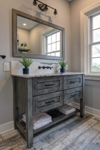 View of an updated bathroom with a wood vanity with a marble countertop and wall-mounted faucet.