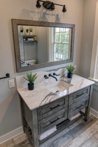 View of an updated bathroom that has been remodeled with a new vanity with marble countertop, wall-mounted faucet, and weathered flooring.