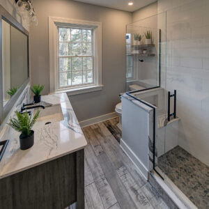 Broad view of an updated bathroom with a vanity with a marble countertop and weathered wood flooring.