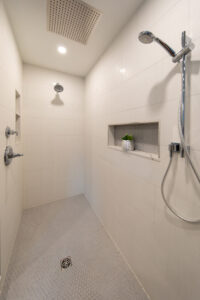 View inside the shower with white tile, a large niche, and multiple faucets.