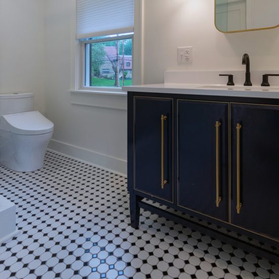 View of a remodeled bathroom with a classic, black and white checkered tile floor, walk-in shower with glass walls, and a large vanity.