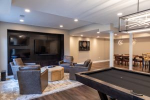 View of the family room in a renovated basement that features an entertainment wall with 3 tvs.