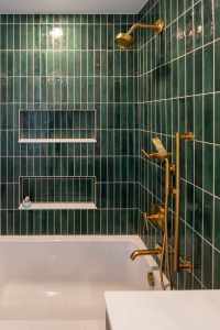 Close up view of the gold fixtures and custom green shower tile in a recently renovated bathroom.