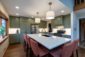 Inviting kitchen with a large island, lots of seating, and green cabinets.
