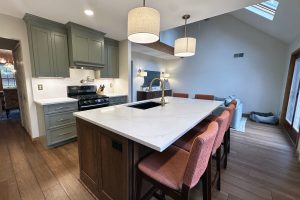 A newly remodeled open concept kitchen with a large island, lots of seating, and green cabinets.
