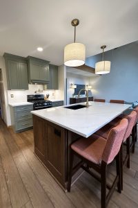 A newly remodeled open concept kitchen with a large island, lots of seating, and green cabinets.