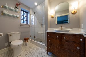 Broad view of master bathroom with stain glass window, wood vanity, and walk-in shower.