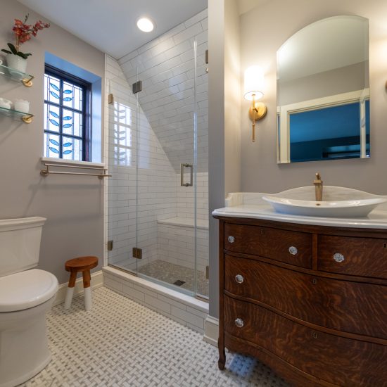 Broad view of master bathroom with stain glass window, wood vanity, and walk-in shower.