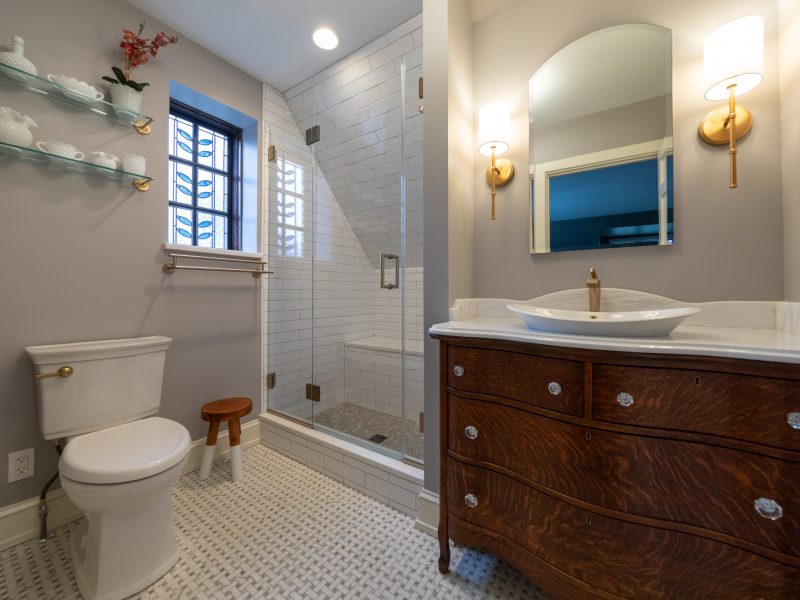 Broad view of master bathroom with stain glass window, wood vanity, and walk-in shower.