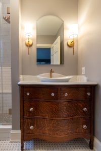 Detailed view of the wood vanity and sconce lighting in a remodeled master bathroom.
