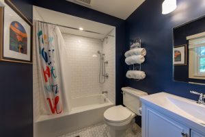 Photo of a remodeled bathroom featuring a white tiled shower, marble floor tile, vanity and toilet.