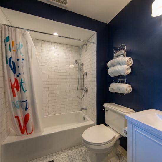 Photo of a remodeled bathroom featuring a white tiled shower, marble floor tile, vanity and toilet.