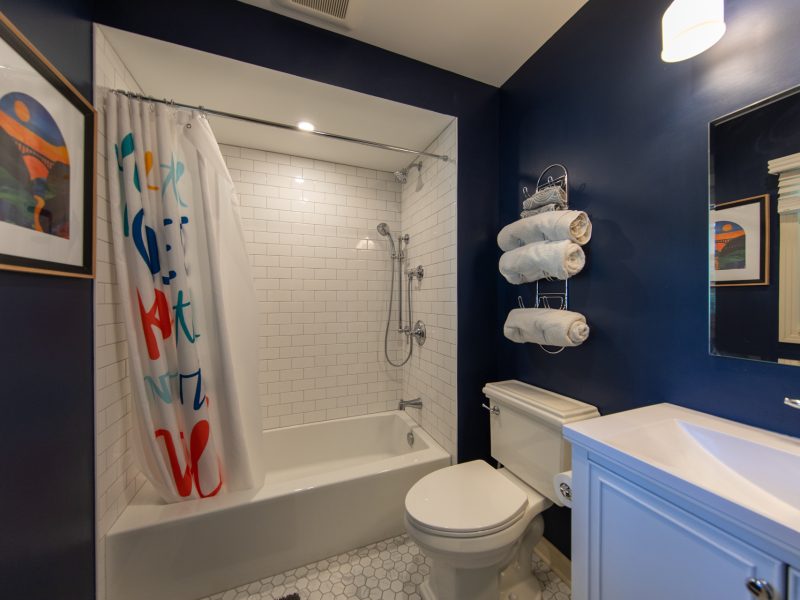 Photo of a remodeled bathroom featuring a white tiled shower, marble floor tile, vanity and toilet.