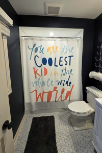 Broad view of a remodeled bathroom featuring a fun and colorful shower curtain, marble floor tile, vanity and toilet.