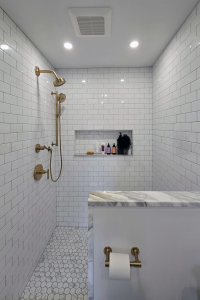 View of a custom tiled shower in a remodeled bathroom. Shower features white subway tile with a custom niche with marble accents and gold hardware.