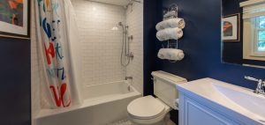 Photo of a remodeled bathroom featuring a white tiled shower, marble floor tile, vanity and toilet.