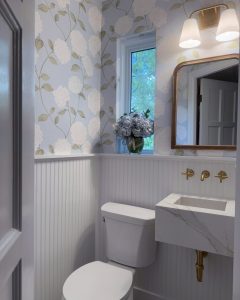 Photo of a recently remodeled powder room with blue floral wall paper, a floating marble sink, and gold fixtures.