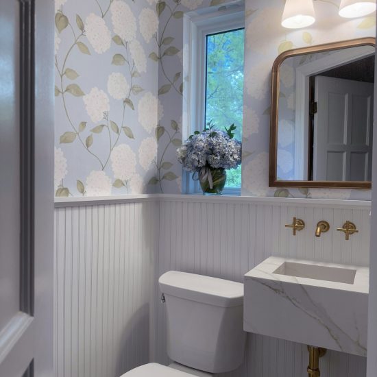 Photo of a recently remodeled powder room with blue floral wall paper, a floating marble sink, and gold fixtures.