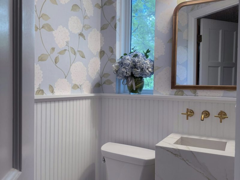 Photo of a recently remodeled powder room with blue floral wall paper, a floating marble sink, and gold fixtures.