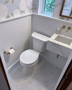 Overhead view of a recently remodeled powder room with blue floral wall paper, a floating marble sink, and gold fixtures.